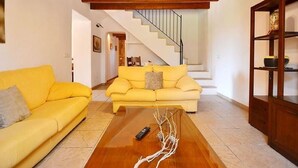 Uma sala de estar com um sofá amarelo, uma mesa de centro de madeira e uma escada que leva a outro andar.