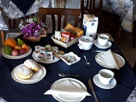 Una mesa de desayuno con platos de pasteles, un frutero, botes de Nutella, una cafetera, tazas y una caja de leche.