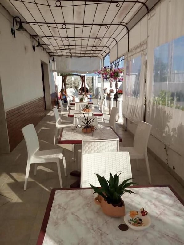 An outdoor patio with white tables and chairs, potted plants, and hanging flower baskets.