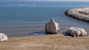 Ein Strand mit großen Felsen, einem klaren blauen Meer und einem felsigen Wellenbrecher.