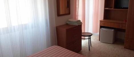 Un dormitorio con cama, cómoda, escritorio con computadora y silla.