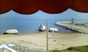 A beach with large rocks, a paved walkway, and a distant view of the sea. - La Scogliera Hotel Boutique (Rodi Garganico)