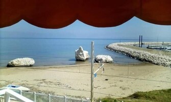 Una playa con rocas grandes, un camino pavimentado y una vista distante del mar.