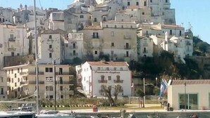 A marina with boats docked, a building with a white facade, and a hillside with multiple buildings. - La Scogliera Hotel Boutique (Rodi Garganico)