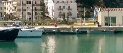 A marina with boats docked, a building with a white facade, and a hillside with multiple buildings.