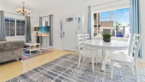 Un salón con sofá, una mesa de centro, un cuadro, una mesa de comedor con sillas y vistas a través de un ventanal.
