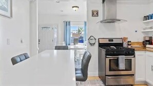 Una cocina moderna con estufa de acero inoxidable, armarios blancos y un comedor con mesa y sillas blancas.