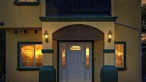 Un edificio de dos pisos con una puerta blanca y dos ventanas iluminadas.
