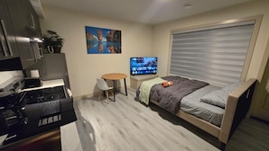 Une chambre compacte comprenant un lit, une petite table, un téléviseur et un coin cuisine.