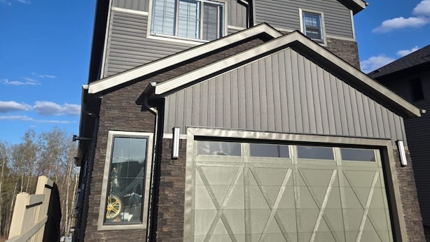 Une maison à deux étages avec un garage, une grande fenêtre et une façade en pierre.