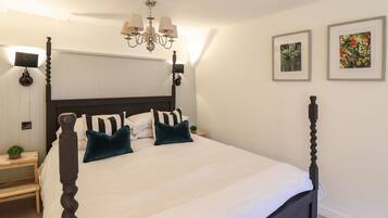 A four-poster bed with a white bedspread and teal pillows, a chandelier, and two framed pictures on the wall.