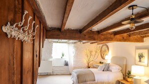 Un dormitorio acogedor con dos camas, techo de madera, una mesita y una ventana con cortinas.