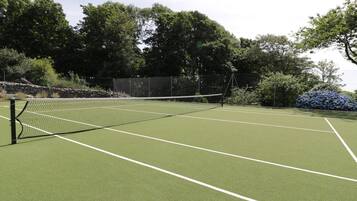 Una cancha de tenis con red, rodeada de árboles y un muro de piedra.