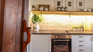 Una cocina con una puerta de madera, un radiador blanco, un horno de acero inoxidable y una repisa con adornos y plantas.
