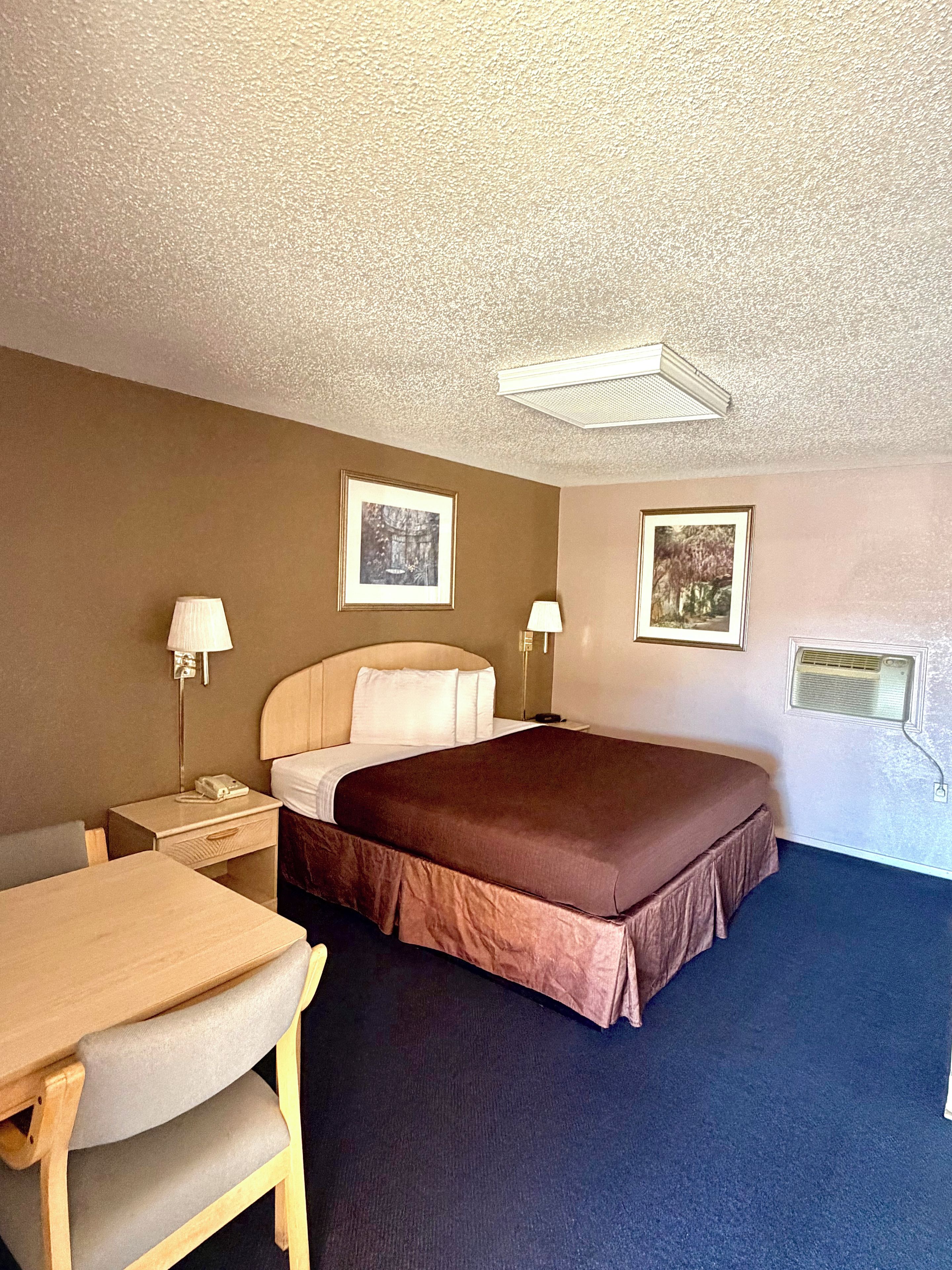 Quarto de hotel com cama, mesas de cabeceira, luminárias e escrivaninha com cadeira.