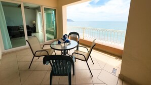 A balcony with a glass door leading to a living area, a round table with chairs, and a view of the sea.