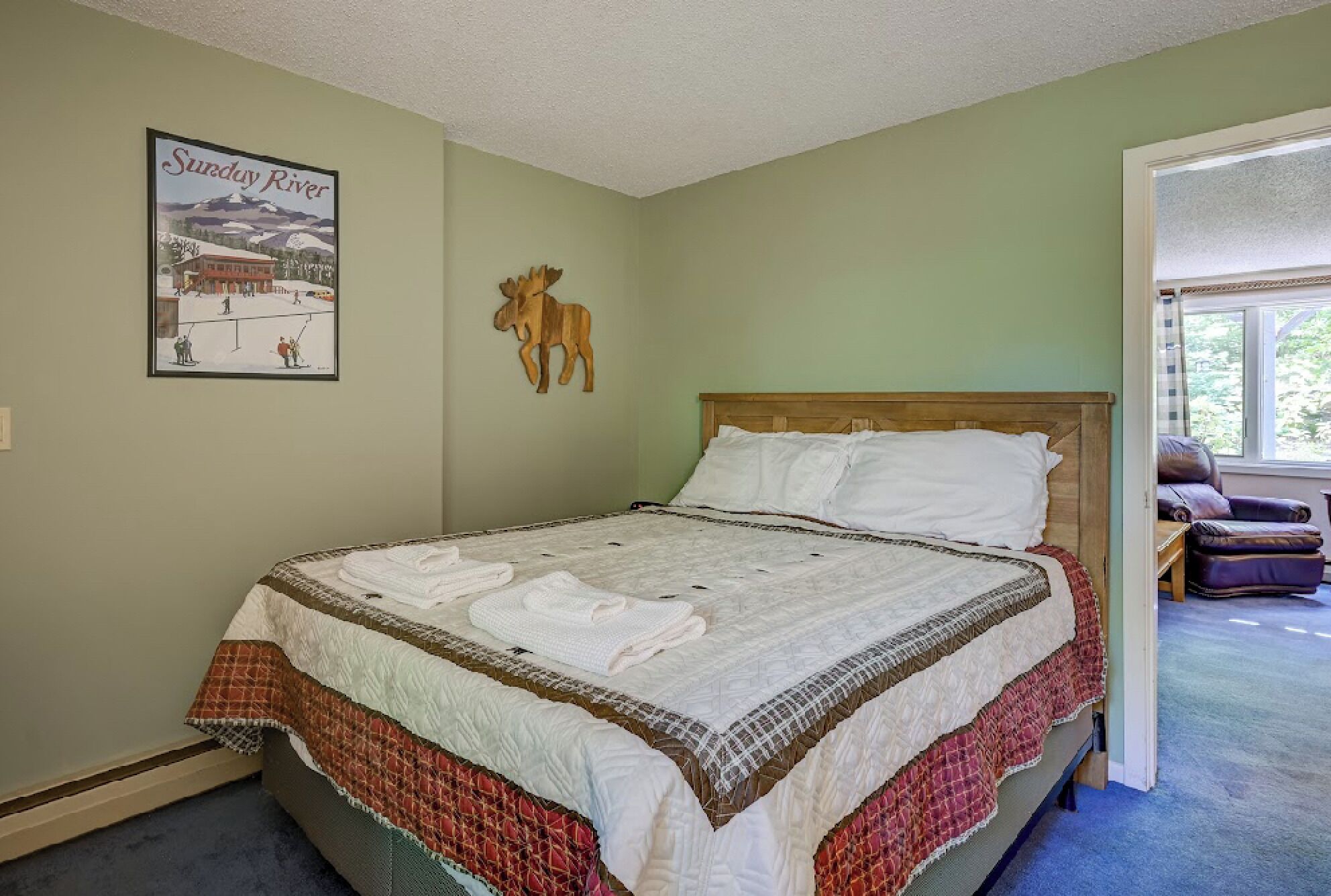 Une chambre à coucher avec un lit, un tableau encadré représentant une station de ski et une tête de wapiti en bois accrochée au mur.