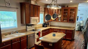 Une cuisine avec des meubles en bois, un îlot central et une fenêtre équipée de stores.