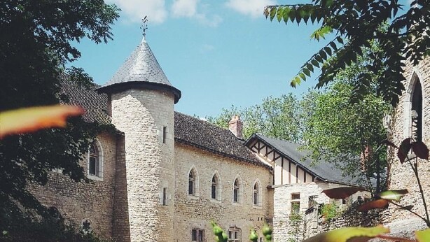 A courtyard with a stone building featuring a tower, surrounded by trees and flowering plants. - Reception hall Champs Forts (Saint-Aoustrille)