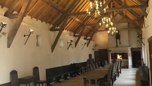 A spacious hall with a high wooden ceiling, a large chandelier, and a long dining table with chairs. - Reception hall Champs Forts (Saint-Aoustrille)