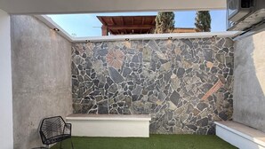 Um pátio moderno ao ar livre com uma parede de pedra, um banco branco e uma cadeira de metal preta.