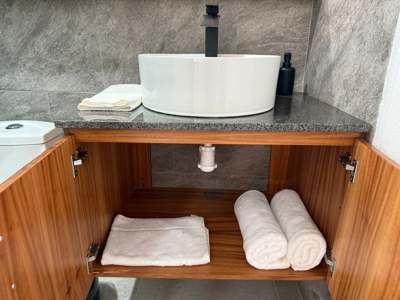 Un baño con tocador de madera, un lavamanos blanco y dos toallas enrolladas.