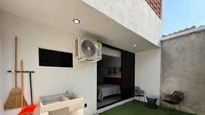 Um banheiro externo moderno com uma pia de concreto, um ventilador de chão e uma vassoura.