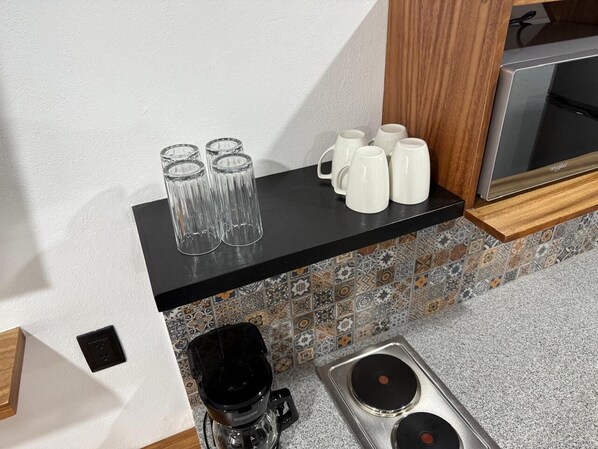 A kitchen with a black countertop, white mugs, and clear glasses.