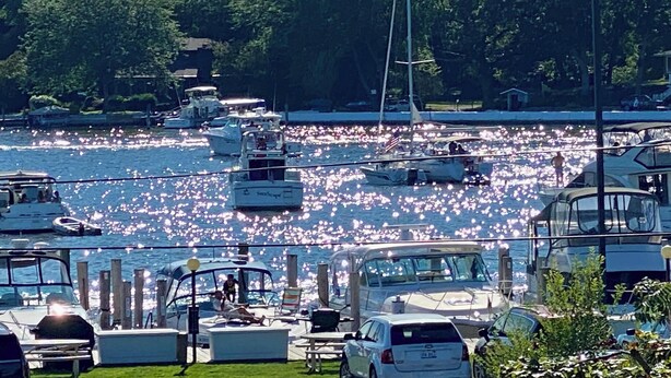 A marina with boats docked, a sailboat, and a row of parked cars.
