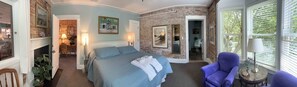 Une chambre à coucher avec un lit, une chaise, un bureau et une salle de bain visible à travers une porte ouverte.