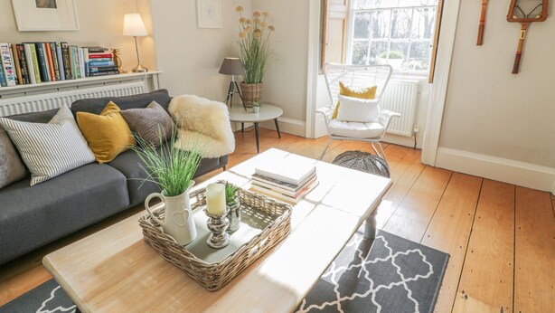 Una sala de estar acogedora con un sofá, una mesa de centro con una cesta, una silla y una ventana con raquetas de tenis en la pared.
