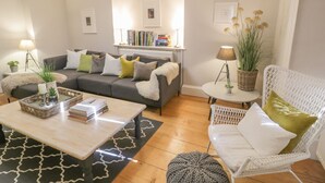 Una sala de estar acogedora con un sofá gris, una mesita de centro, una silla blanca y una estantería llena de libros.
