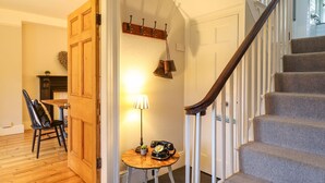 Una escalera con barandilla de madera y peldaños alfombrados, una puerta de madera, una mesa con lámpara y una silla.