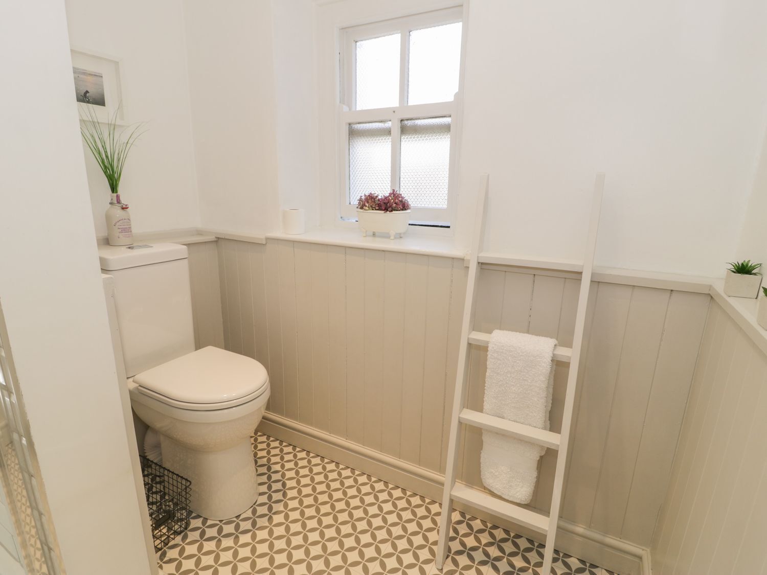 A bathroom with a toilet, a window with a view, a towel rack, and patterned floor tiles.
