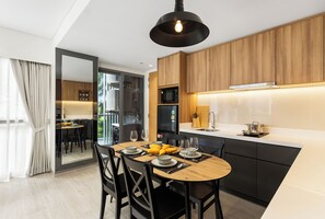 A modern kitchen with wooden cabinets, a central island, and a dining area with a round table and chairs. - Lakeside BangTao by My Home Phuket (Choeng Thale)