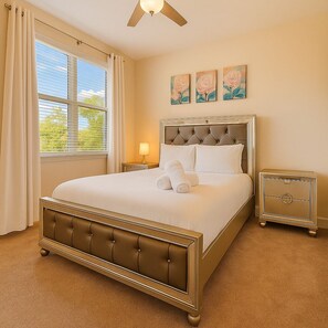 A well-lit bedroom with a large bed, a nightstand, a bedside table, and a wall-mounted artwork.
