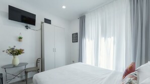 Une chambre d’hôtel avec un lit, un téléviseur fixé au mur, une petite table avec un vase de fleurs et une armoire.