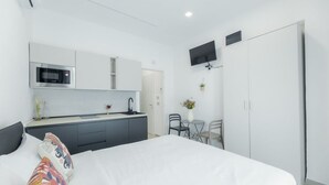 Une chambre moderne avec un grand lit, une petite kitchenette équipée d’un four à micro-ondes et un téléviseur fixé au mur.