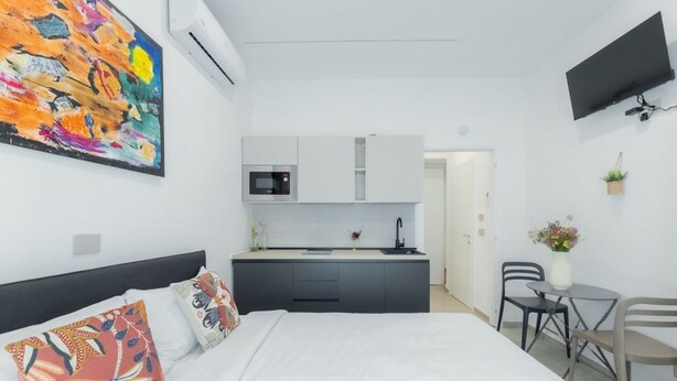 Une chambre d’hôtel moderne équipée d’un lit, d’une petite kitchenette, d’un coin repas et d’un téléviseur fixé au mur.