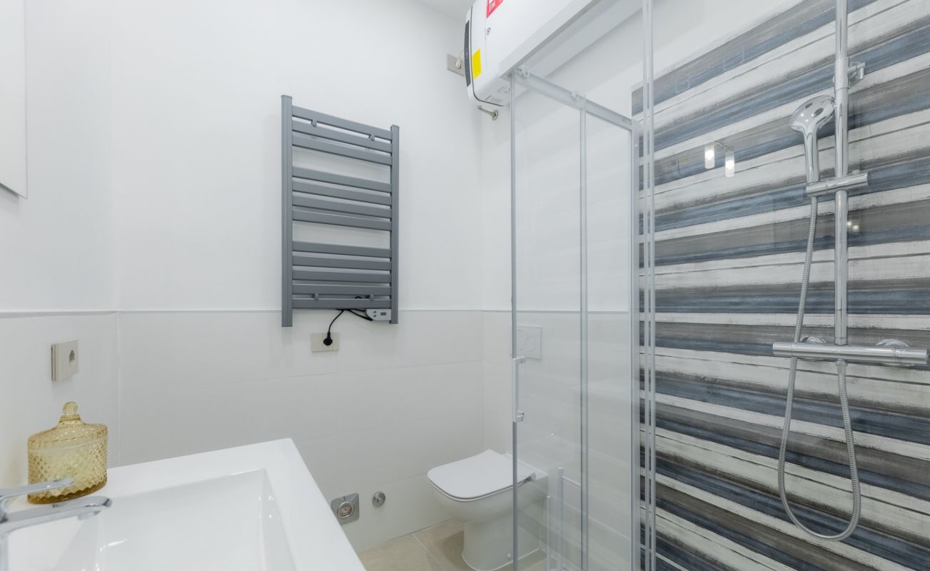 Ein modernes Badezimmer mit einem weißen Waschbecken, einer Glasdusche und einem Handtuchhalter.