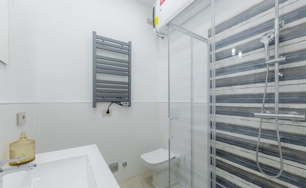 Un baño moderno con un lavamanos blanco, cabina de ducha con mampara de vidrio y un perchero para toallas.