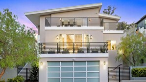 Une maison moderne à deux étages, dotée d’un garage, d’un balcon et d’un éclairage extérieur.