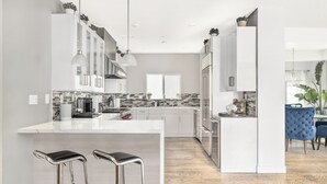 Une cuisine moderne avec des meubles blancs, un îlot central doté de tabourets de bar et un coin repas avec des chaises bleues.