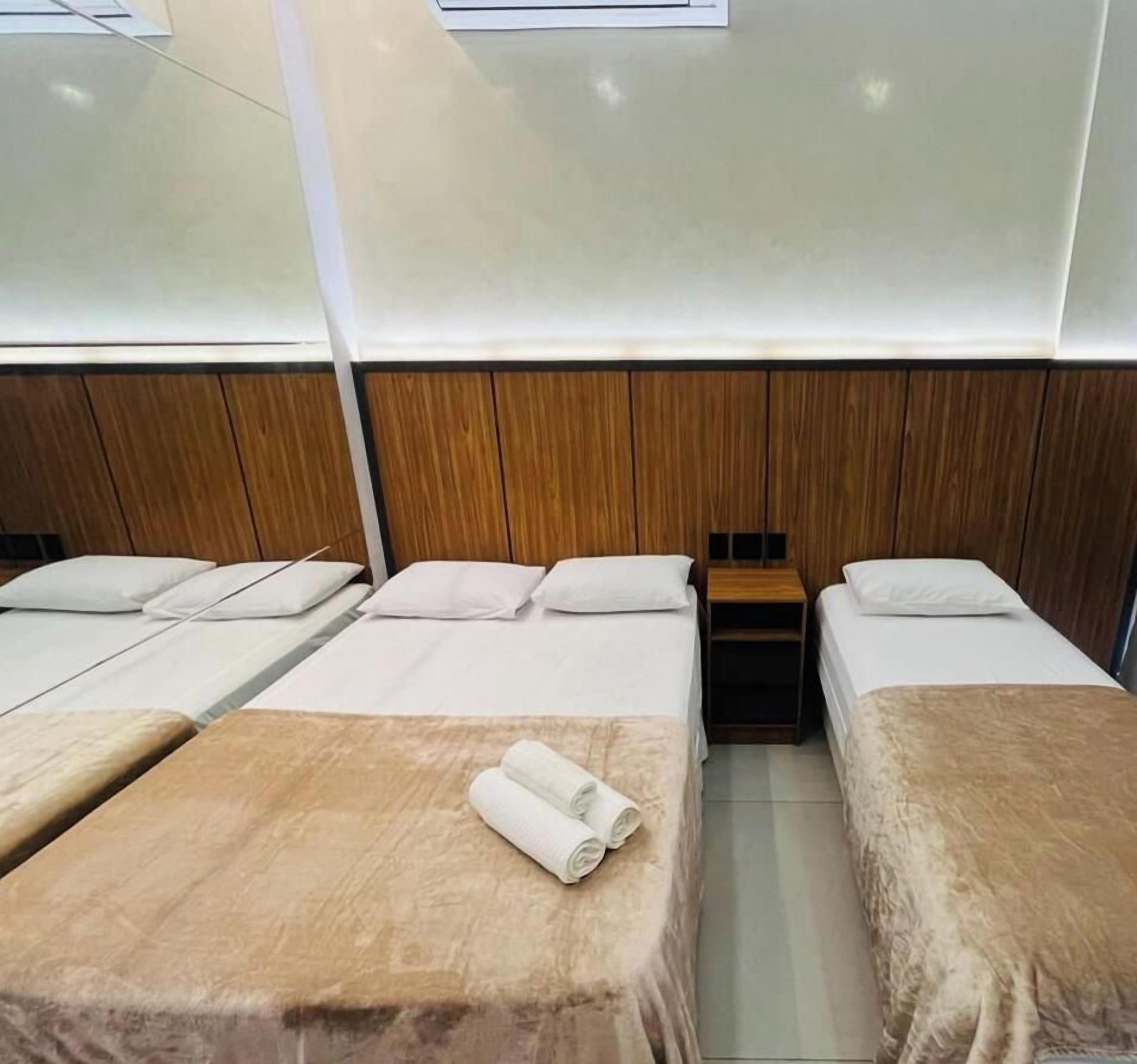 A hotel room with four beds arranged in a row, a wooden headboard, and a small wooden table between the beds.