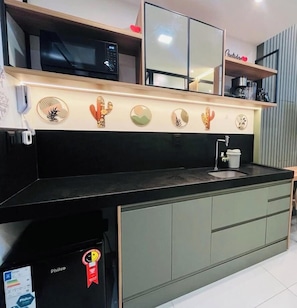 Une cuisine avec un plan de travail noir, un évier et un micro-ondes placé au-dessus. On y trouve une étagère avec une machine à café et une décoration en forme de cœur rouge.
