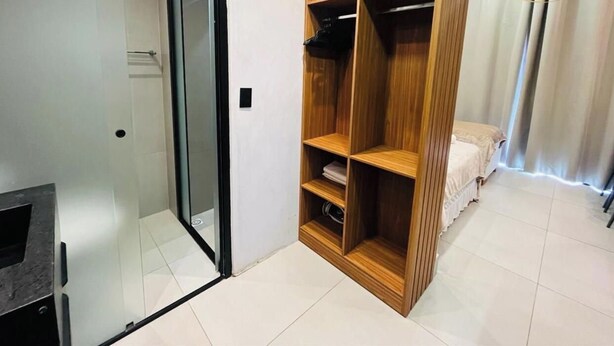 A room with a glass door leading to a bathroom, a wooden wardrobe, and a bed with a white duvet. - LM GET SENSE PE NA AREIA (Joao Pessoa)