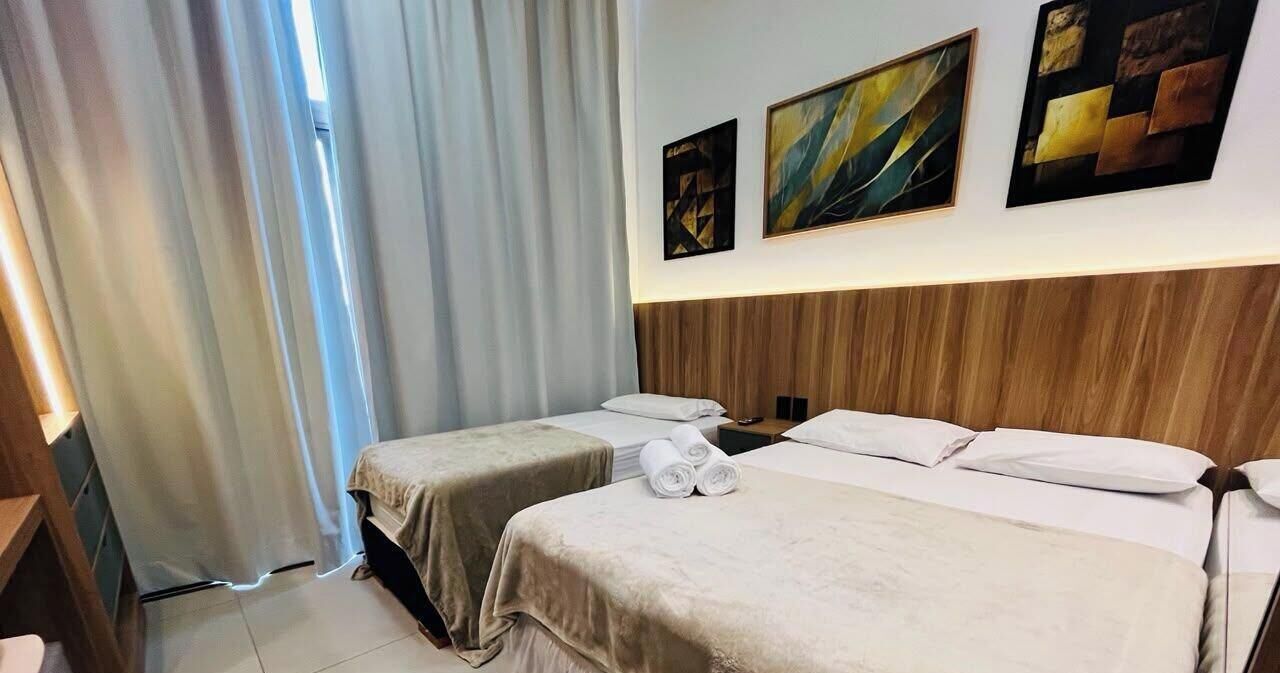 Quarto de hotel com duas camas, cabeceira de madeira e obras de arte na parede.