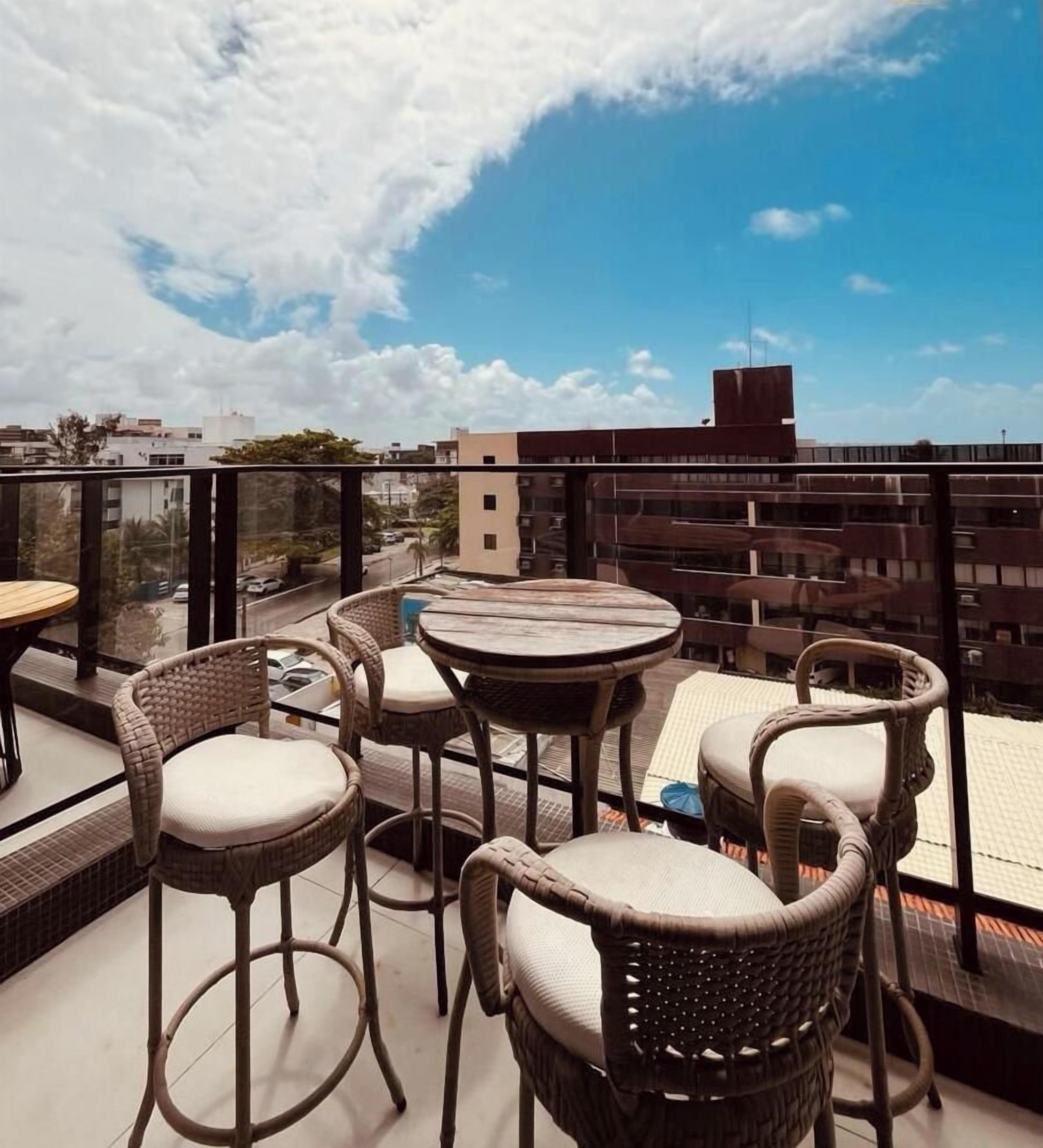 A rooftop terrace with wicker furniture, a round table, and a view of the cityscape.