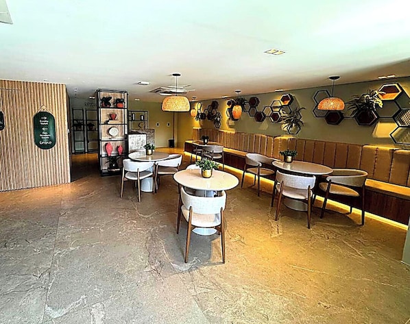 L’intérieur d’un restaurant avec des tables rondes, des chaises, un séparateur en bois et un mur orné de motifs hexagonaux.