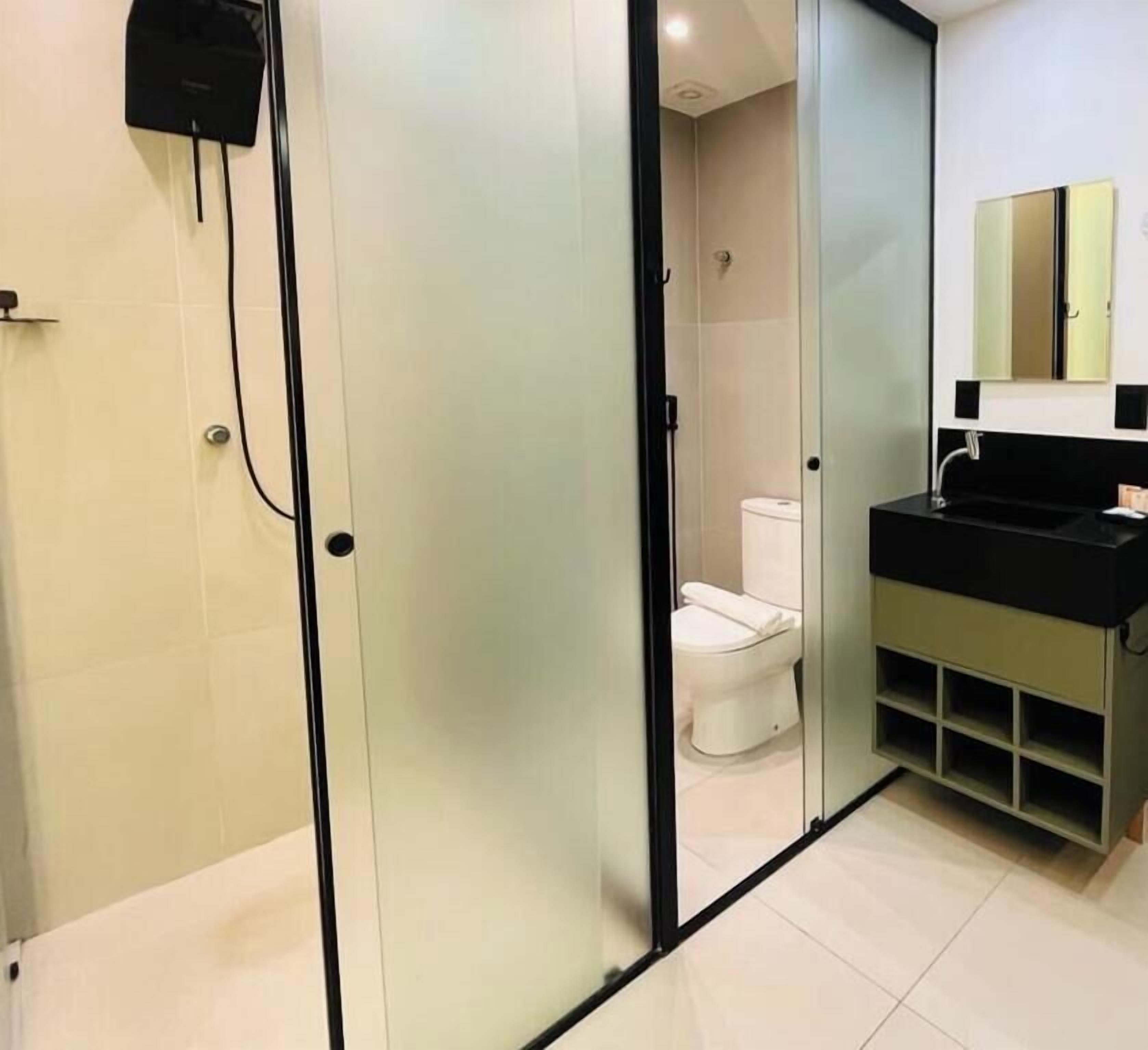 Un baño moderno con mampara de vidrio, lavamanos negro y un inodoro visible a través de la mampara.